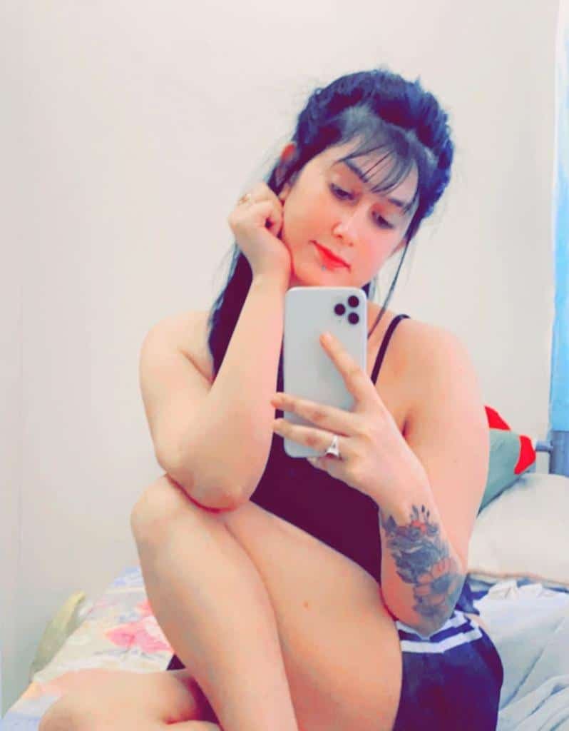 A woman sitting on a bed, looking at her phone with a thoughtful expression.